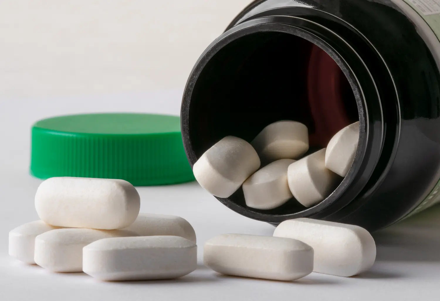 hands holding a white supplement tablet and a glass of water